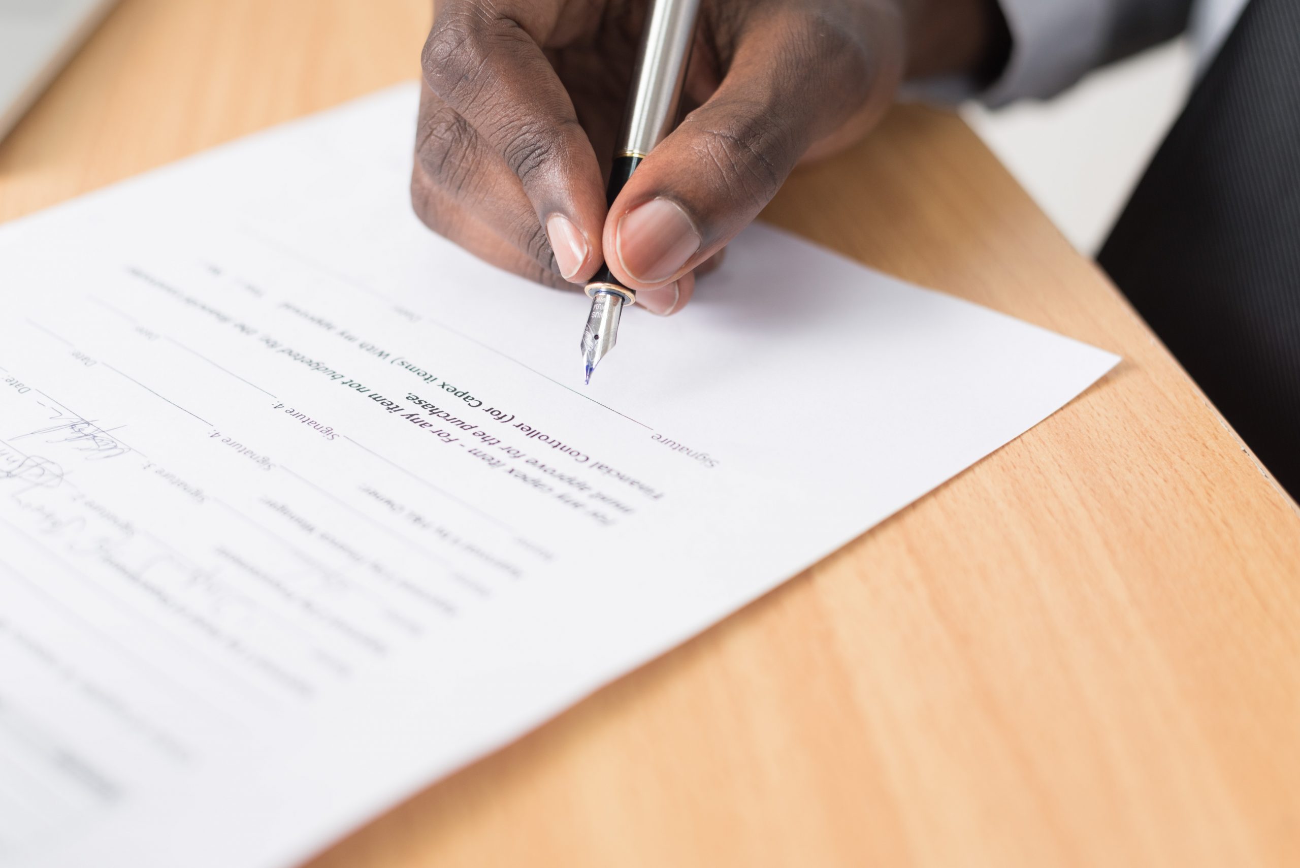 black person's hand signing a document with fountain pen